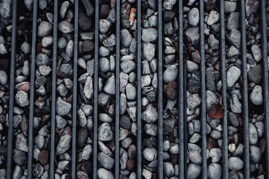 Close-up of a linear channel drain grate set into gravel at the edge of a hard surface