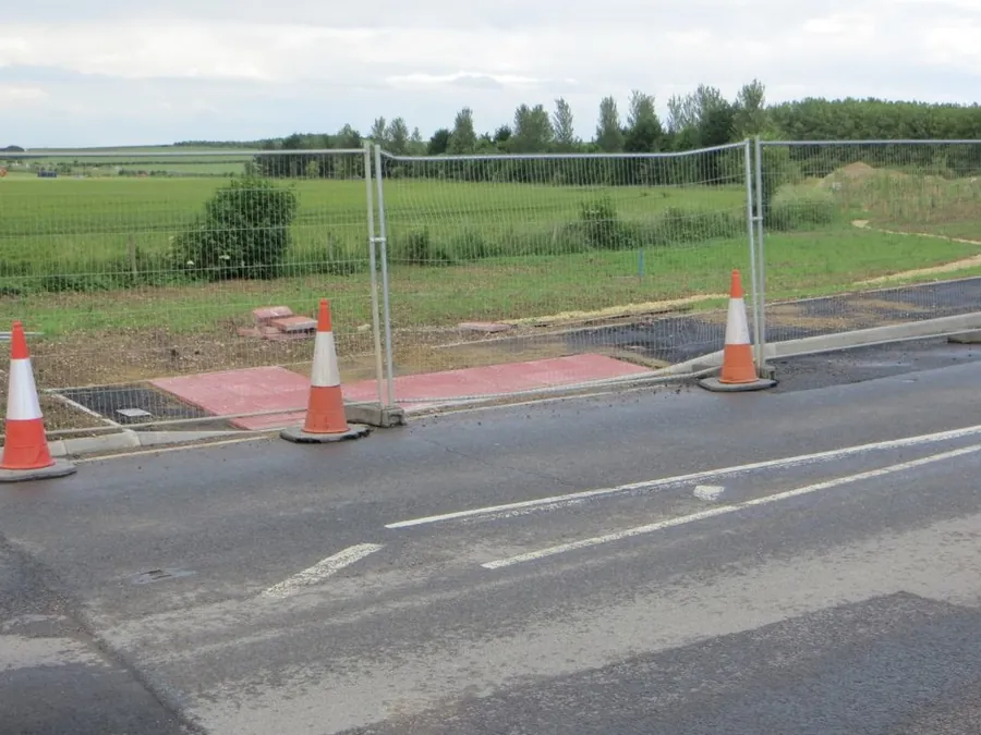 Newly built dropped kerb and red block crossover across a pavement, coned off while it sets