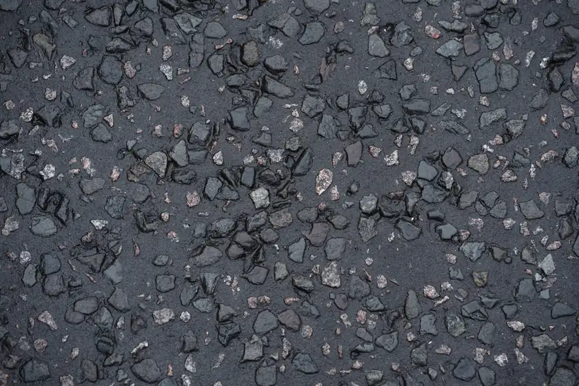 Close-up of a tarmac surface with loose stone chippings worked free of the bitumen